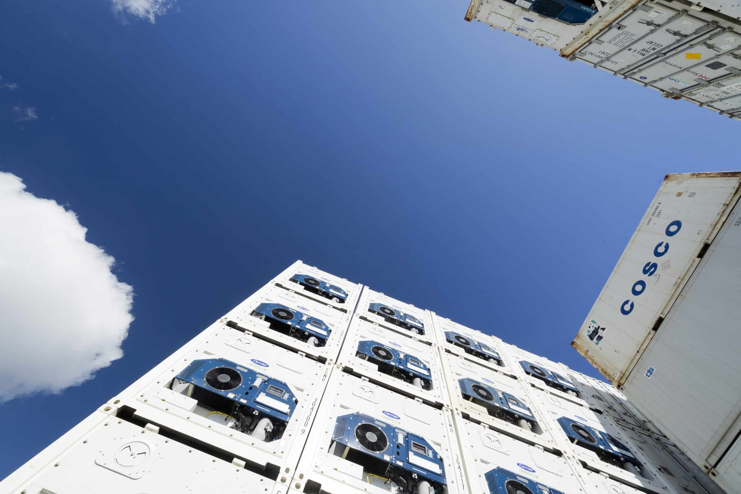 Blue sky and clouds seen through stacked shipping containers.