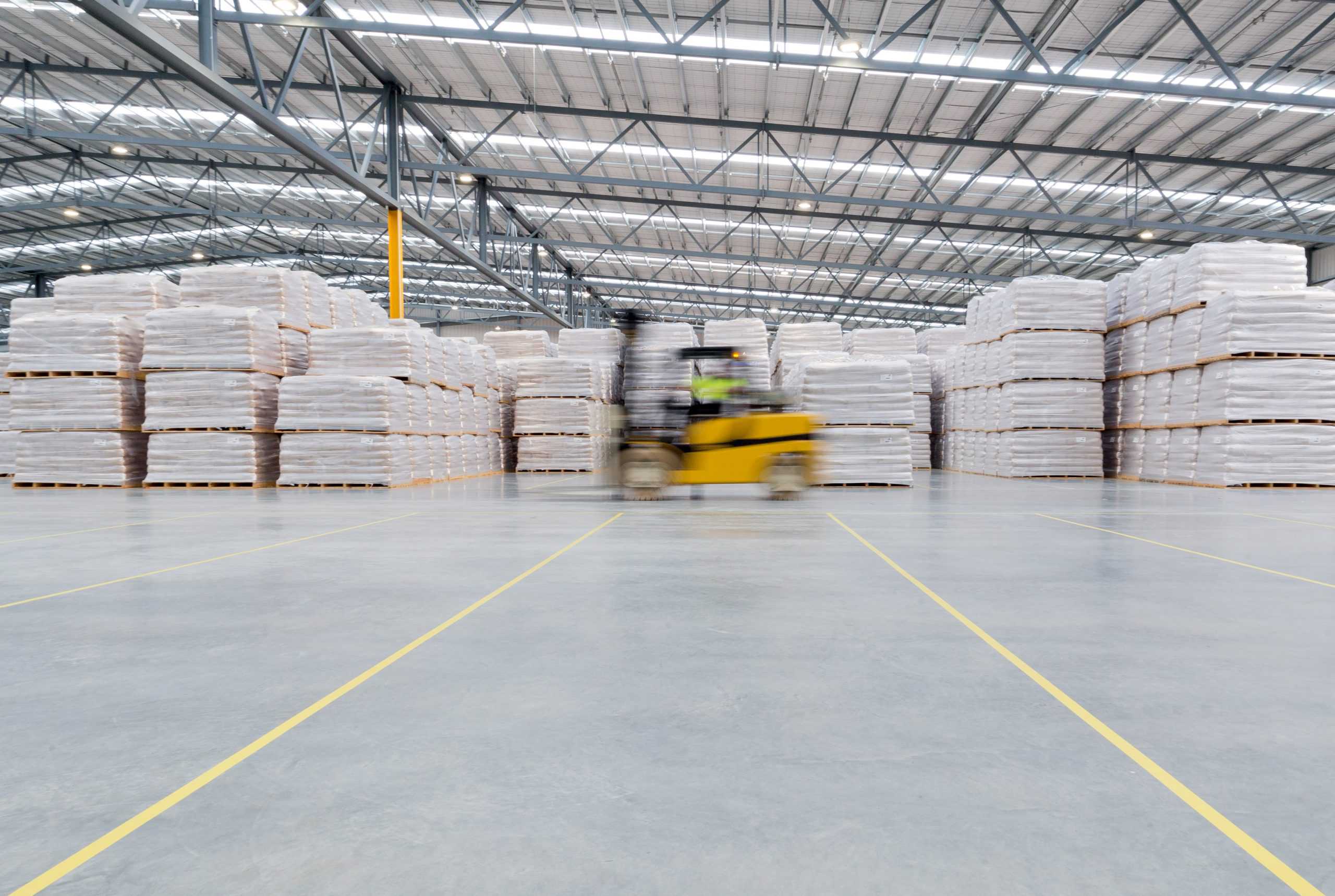 Forklift blurs as it moves past stacked milk products in factory warehouse.
