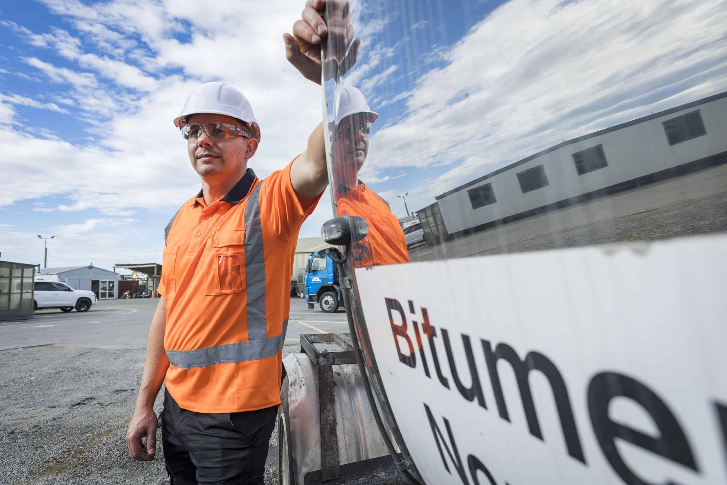 Model with PPE leaning against bitumen tanker, Christchurch.