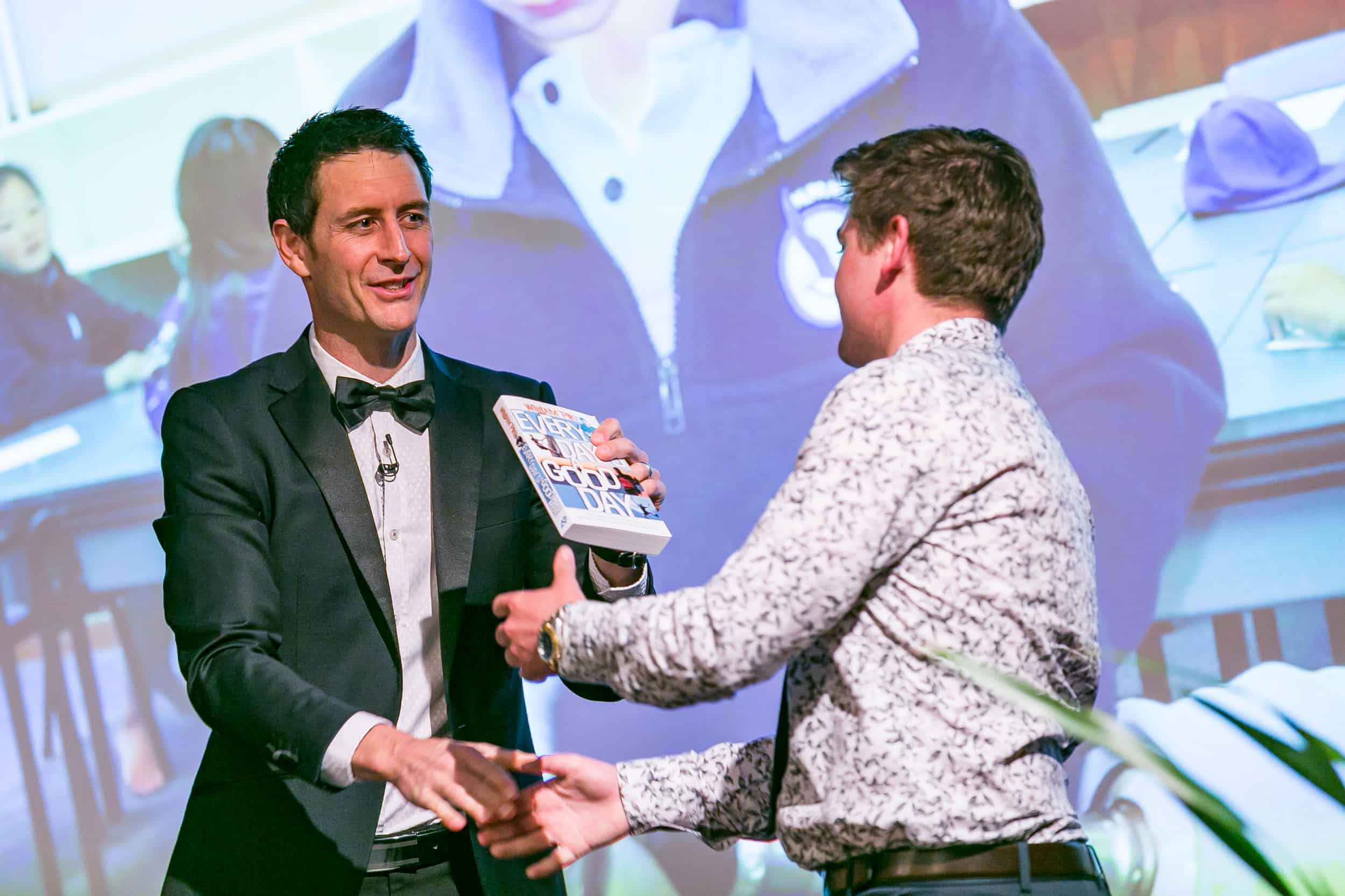 William Pike presents winner with book on stage during conference session, Christchurch Town Hall.