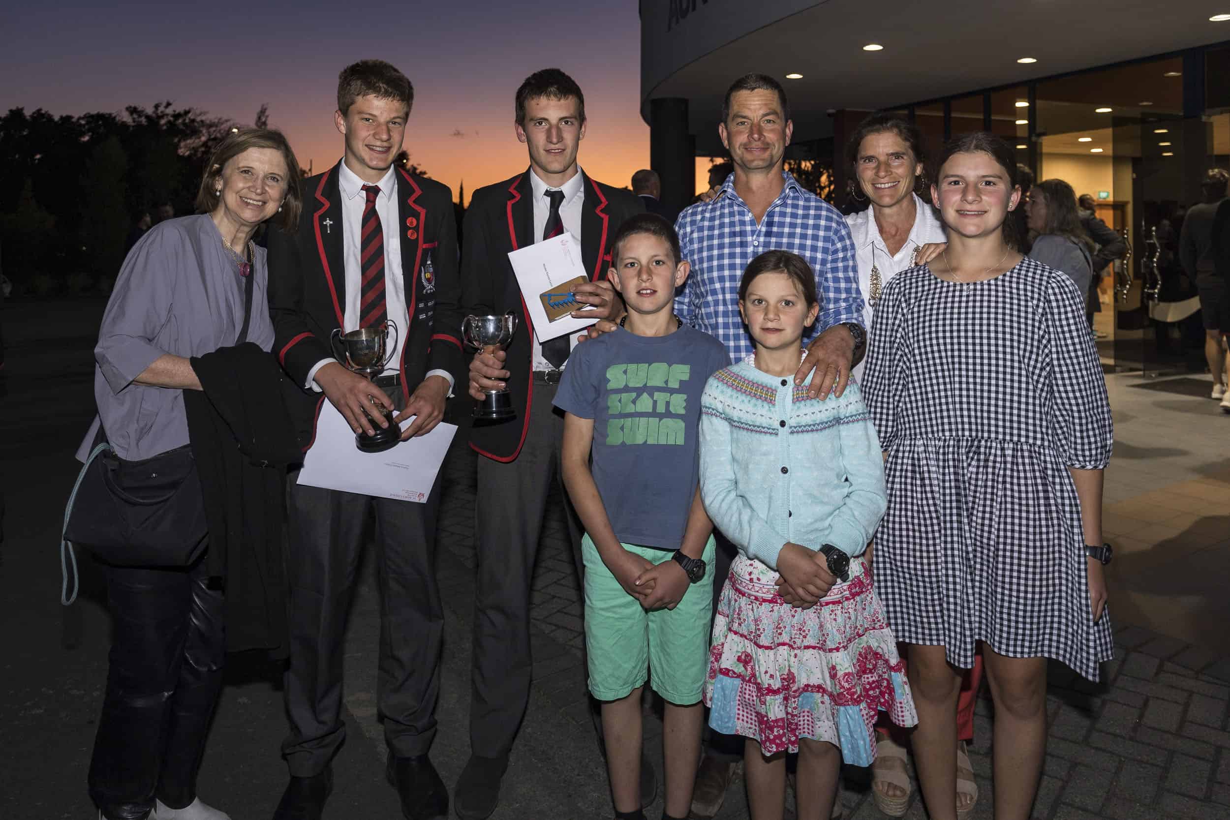 Family outside auditorium at dusk with their son after receiving an award at a school presentation.