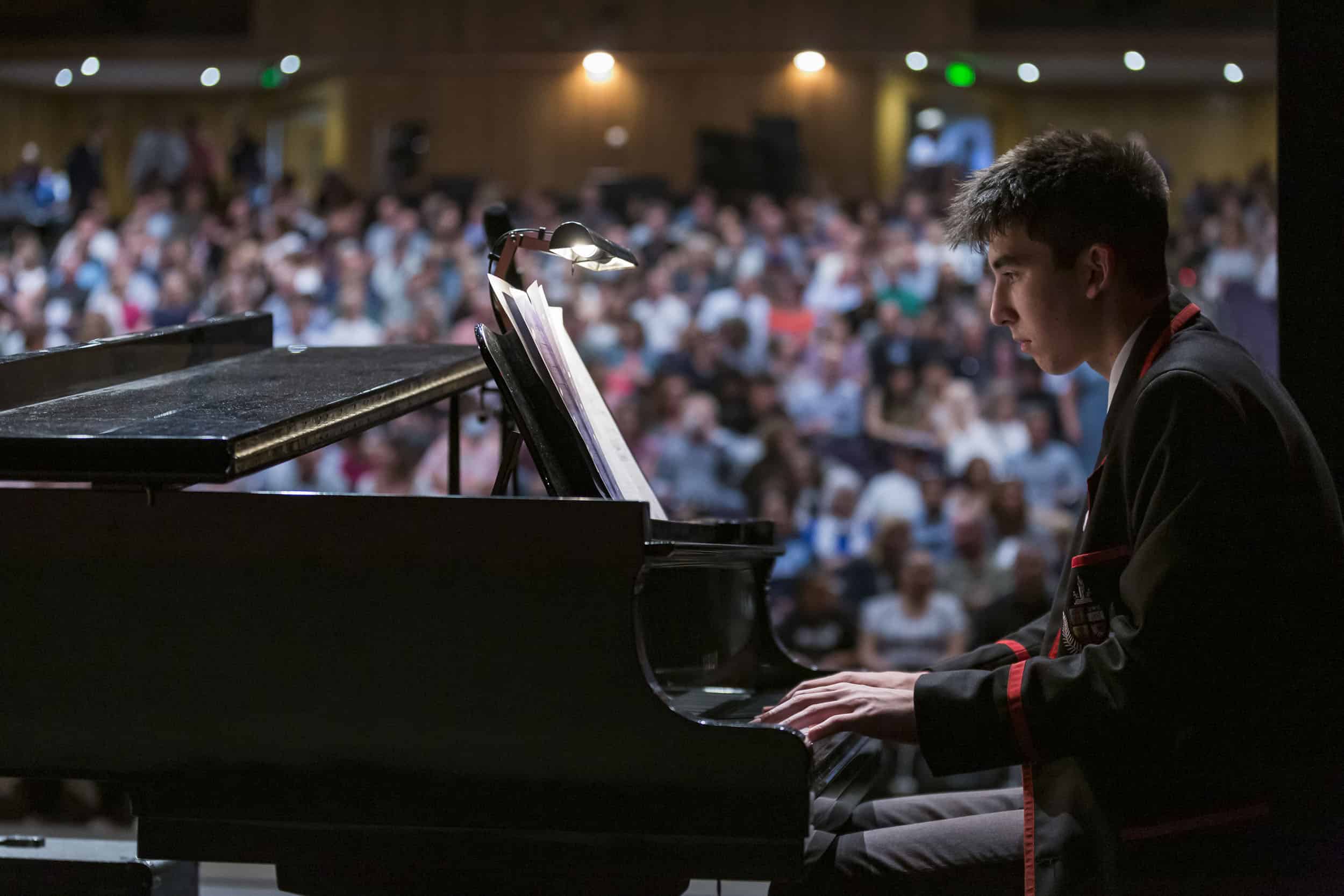 Male high school student performs a piano recital on stage at an awards function.
