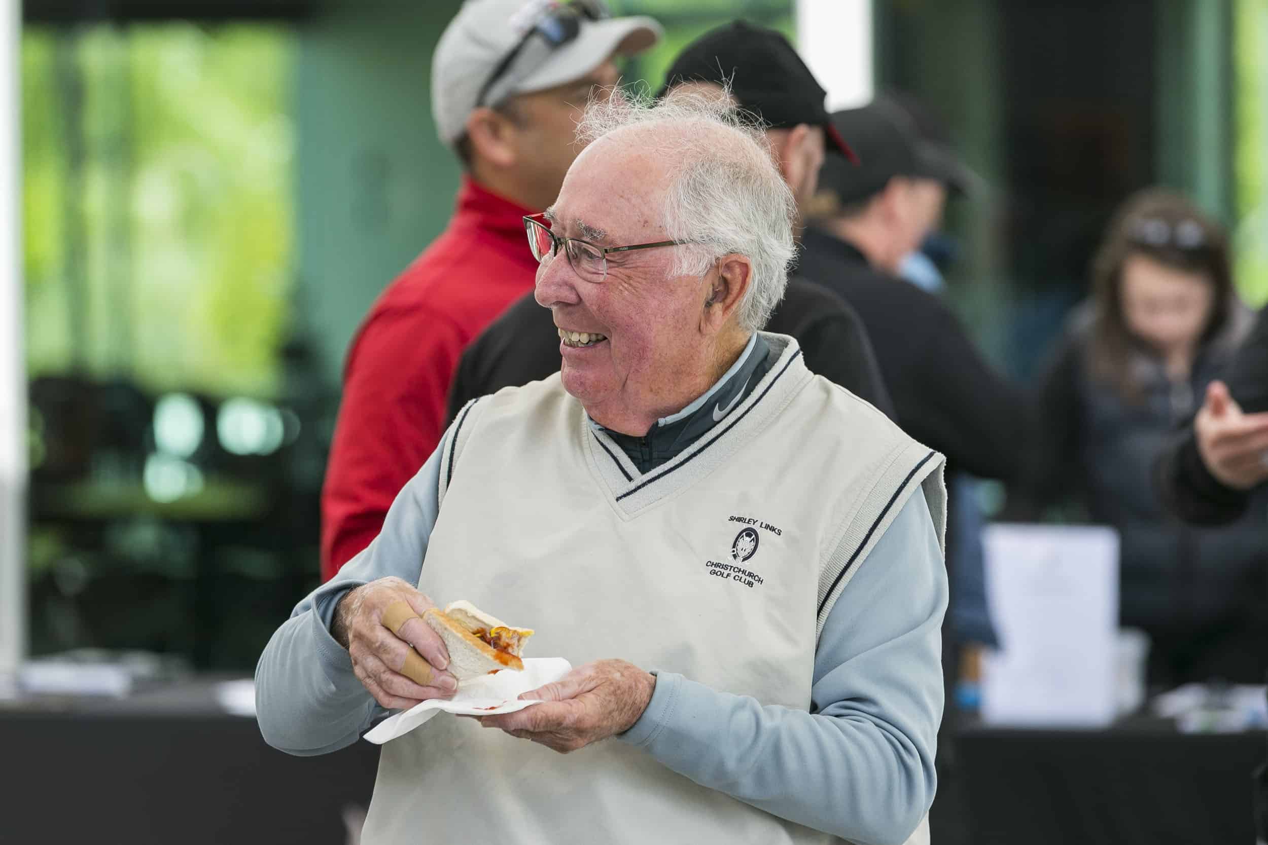 Golfer enjoying sausage in bread at charity match.
