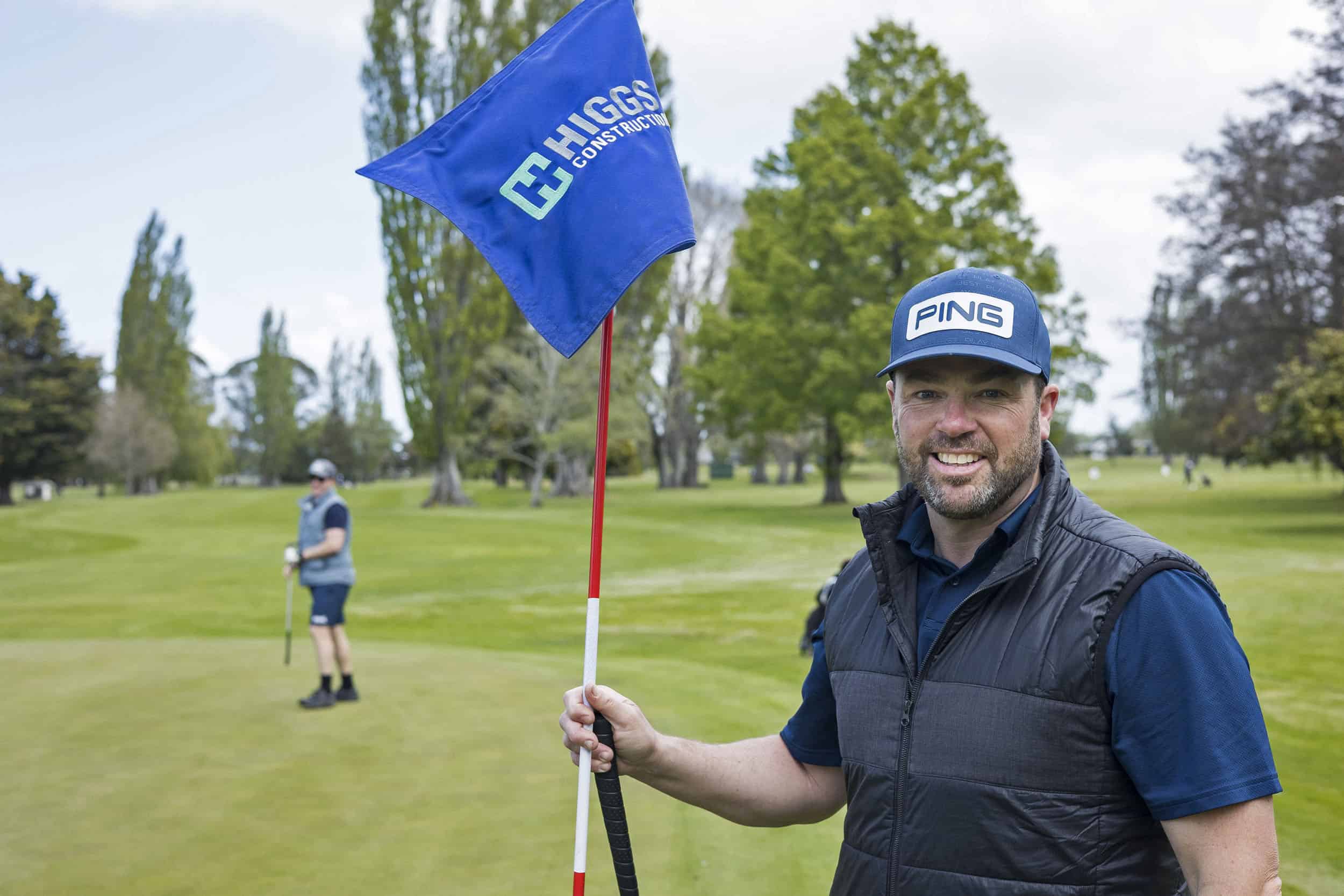 Happy golfer holds flag for colleague at a corporate golf tournament.