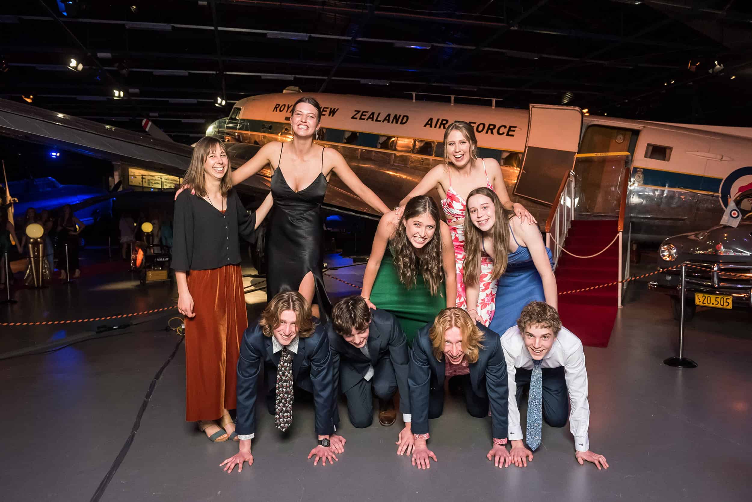 Nearly a pyramid as students attempt to go higher posing for photos at their school ball, Wigram Air Force Museum, CHCH.